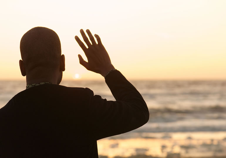 夕日が沈む海に手を振る男性