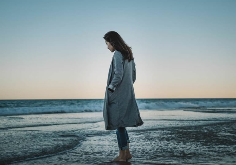 浜辺でコートを羽織り海を見つめる女性