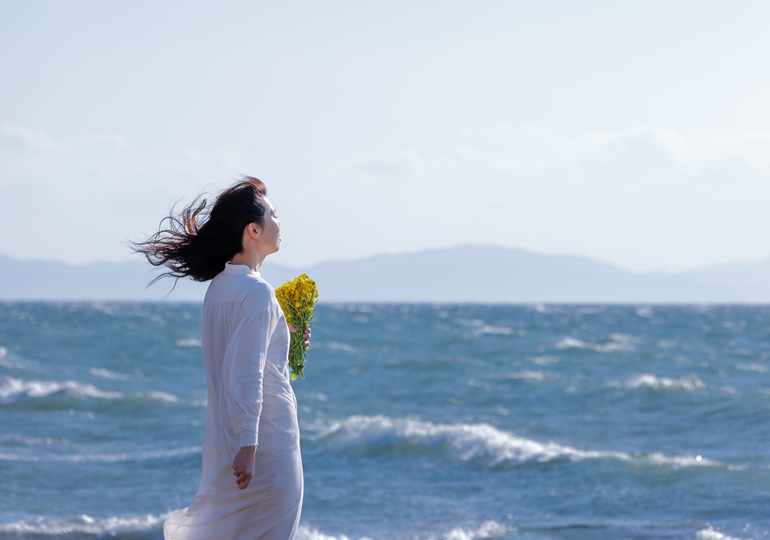 花束を持って浜辺に佇む女性