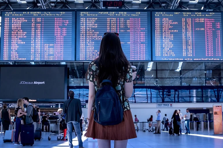 空港の案内表示を見つめて世界に飛び立つ決意をした女性の後ろ姿
