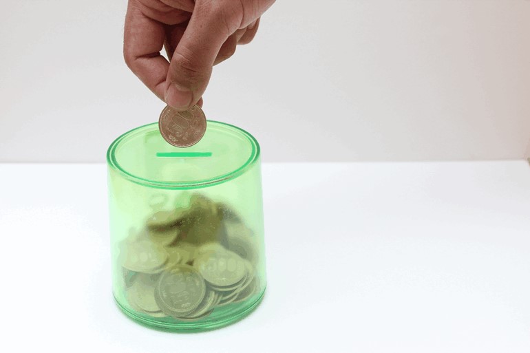 貯金箱に500円玉を入れている男性の手元