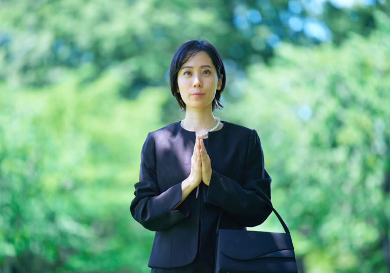 喪服で永代供養墓に合掌する女性