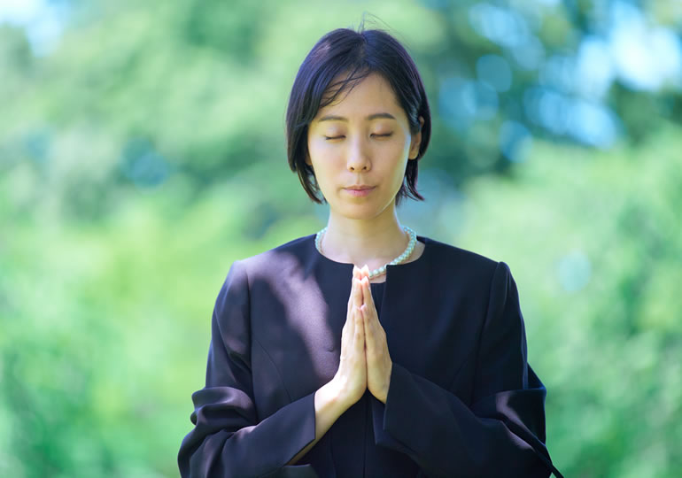 喪服姿で手を合わせる女性