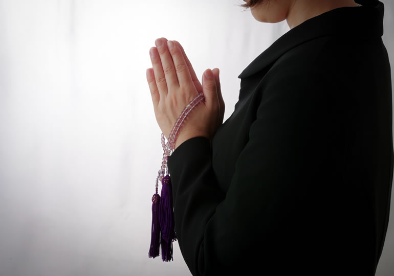 数珠を持って手を合わせる女性