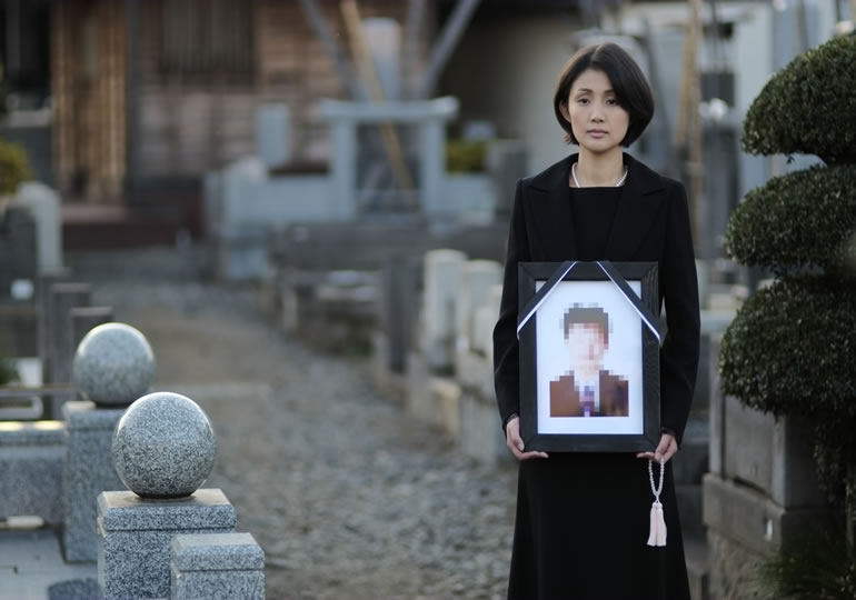 墓地で喪服姿で夫の遺影を持つ女性